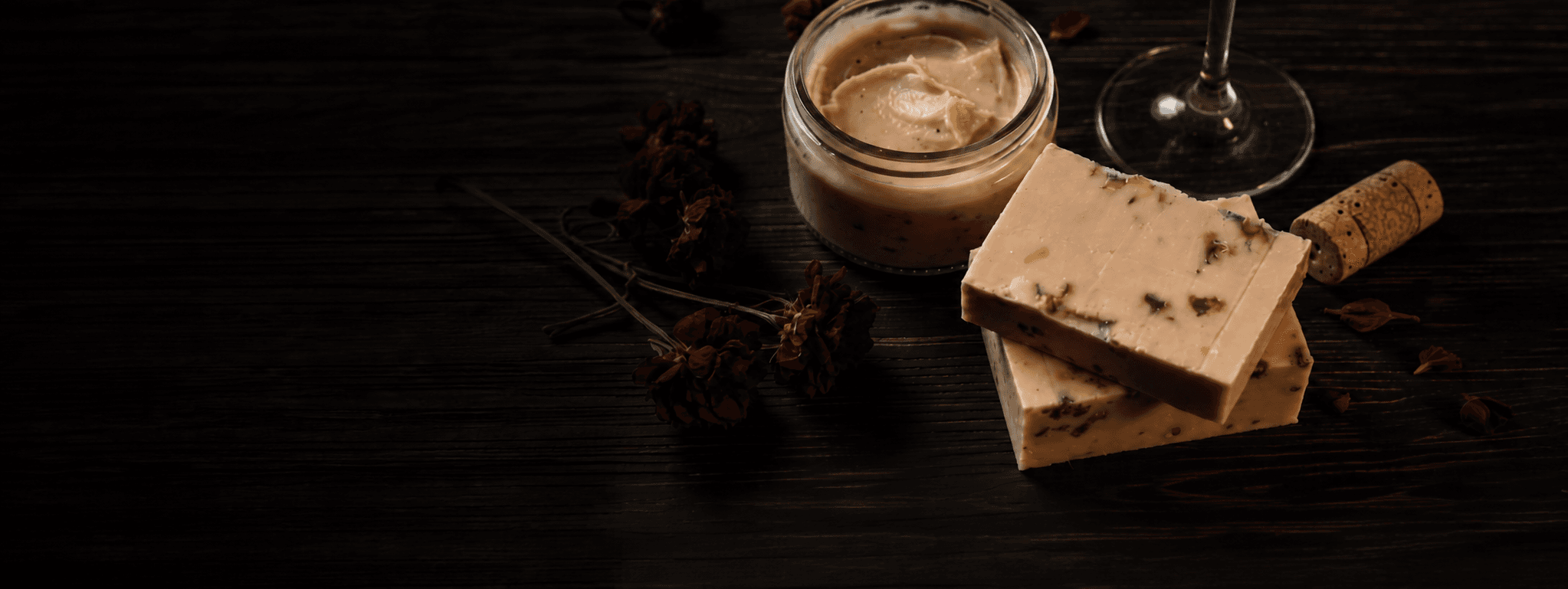 Wine, handcrafted body butter, soap, and dried botanicals arranged on dark wood